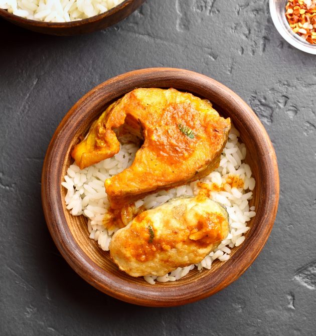 Delicious fish curry with rice in wooden bowl on black stone table. Indian style food. Top view, flat lay